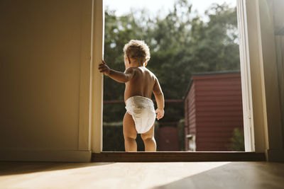 Full length of shirtless man standing by window at home