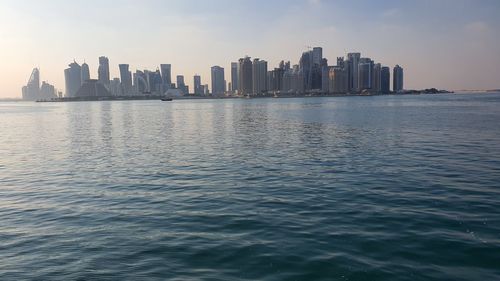 Sea by buildings in city against sky