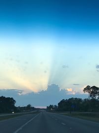 Road by silhouette trees against sky during sunset