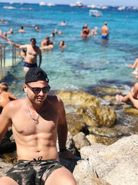 Full length of shirtless man on rocks at sea shore