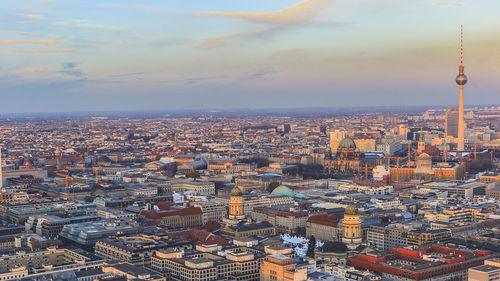 Fernsehturm amidst cityscape against sky during sunset