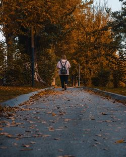 Rear view of woman walking on sidewalk during autumn