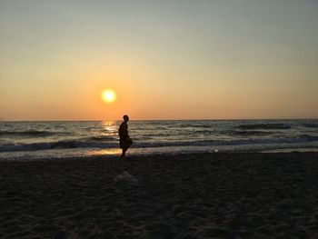 Silhouette woman on beach against sky during sunset