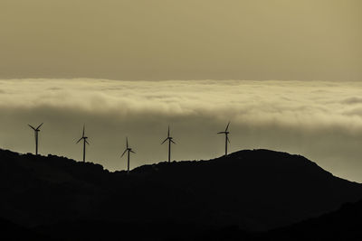 Windmills on silhouette landscape against sky during sunset