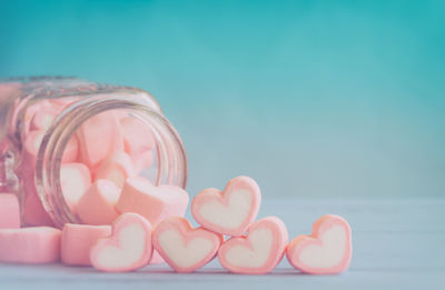 Close-up of heart shape marshmallows spilling from glass jar against blue background