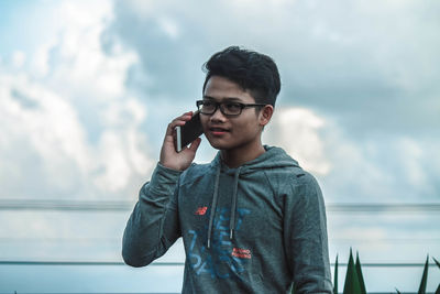 Young man talking on mobile phone against sky