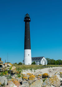 Lighthouse by sea against clear blue sky