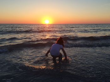 Rear view of woman standing on beach against sky during sunset