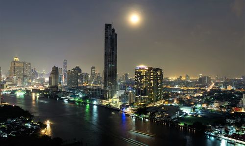 Illuminated buildings by river against sky in city at night