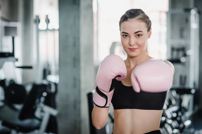 Portrait of young woman wearing boxing gloves in gym