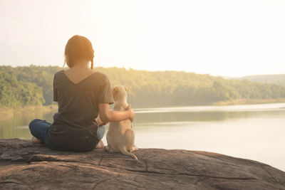 Young couple sitting on lake against clear sky
