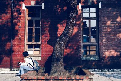 Woman sitting by building in city