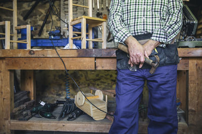 Midsection of man holding hammer while standing by table