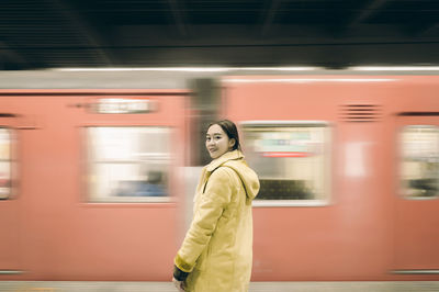 Portrait of woman standing against train moving at railroad station