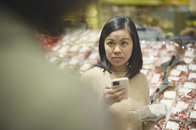 Woman standing in supermarket and holding cell phone