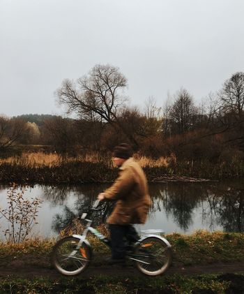 Side view of man riding bicycle by lake against sky