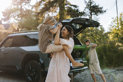 Smiling woman playing with son while standing in front of car