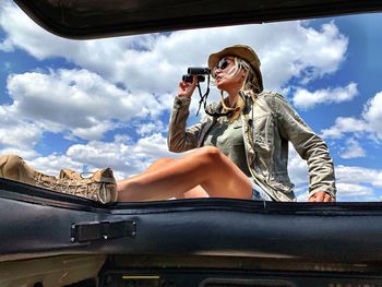 Full length of woman sitting on jeep against cloudy sky