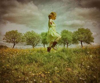 Side view of girl walking on grassy field against cloudy sky