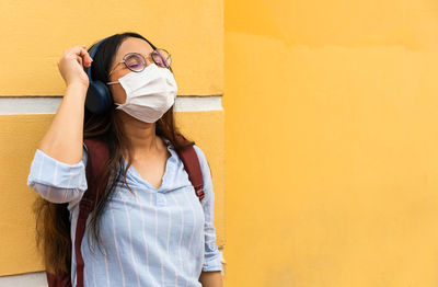 Full length of young woman standing against yellow wall