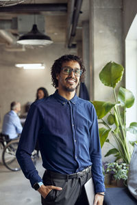 Portrait of smiling businessman standing with laptop at creative office