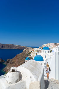 Woman taking snap of santorini, with typical blue dome church, old whitewashed houses and caldera