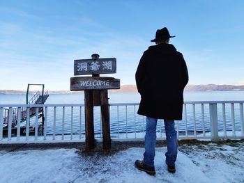 Rear view of man standing at lakeshore during winter