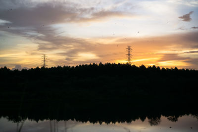 Silhouette trees and electricity pylon against sky during sunset