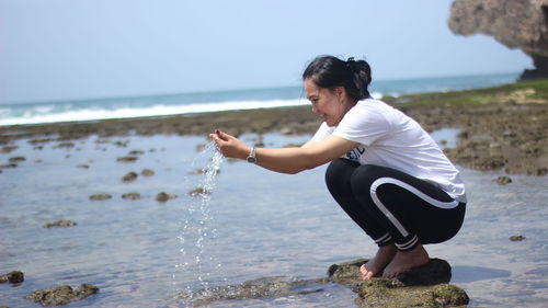 Full length of woman playing with water at beach