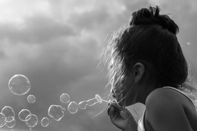 Close-up of girl blowing bubbles against sky