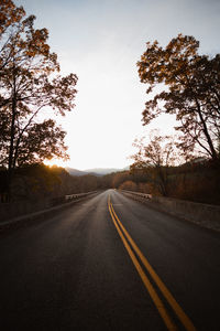 Empty road along trees and against sky