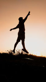 Silhouette man jumping on field against sky during sunset