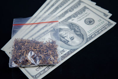 Close-up of marijuana on paper currency over black background