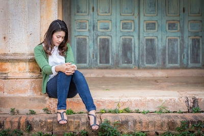 Full length of teenage girl sitting outdoors