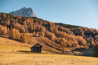 House on field by mountain against clear sky