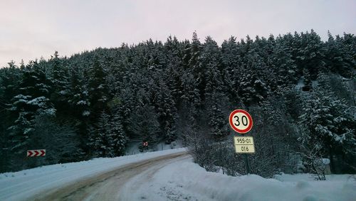 Road sign by snow covered trees against sky