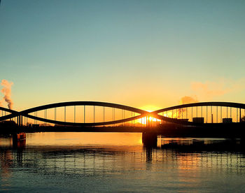 Silhouette bridge over river against sky during sunset