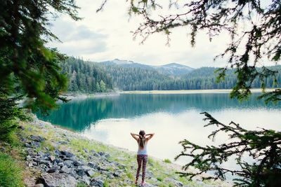 Rear view of woman standing at lakeshore against sky