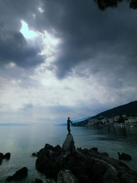 Man standing on rock by sea against sky