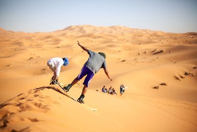 People sandboarding in desert against clear sky