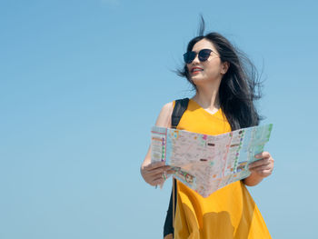 Young woman wearing sunglasses standing against clear blue sky