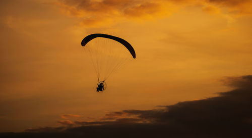 Low angle view of person paragliding against sky during sunset