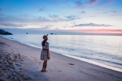 Woman standing on beach against sky during sunset