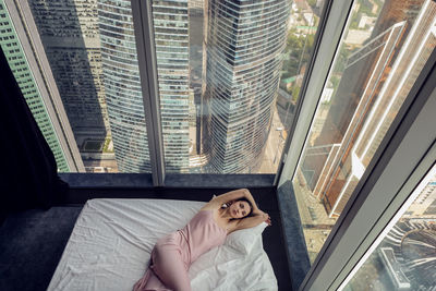 Woman in a nightgown lying on the bed window in a skyscraper near the bed