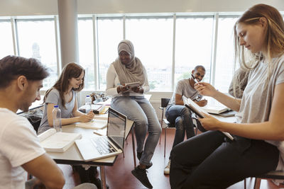 Smiling multi-ethnic friends discussing over project in classroom at university