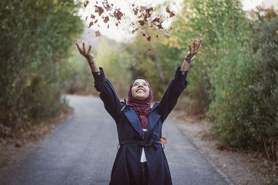 Full length of woman with arms raised standing on road