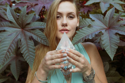 Portrait of young woman holding prism while standing against plant