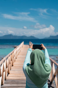 Outdoor portrait of woman in hijab taking photo of the scenery with her smartphone.