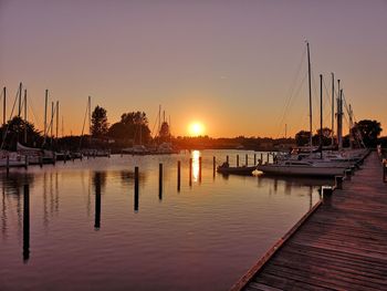 Sailboats moored at harbor against clear sky during sunset