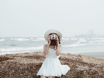 Portrait of young woman photographing with camera at beach